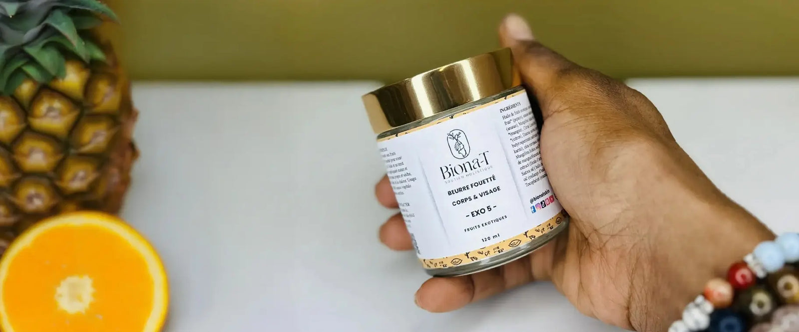 une main qui tient un beurre fouetté corps et visage avec un ananas et une orange